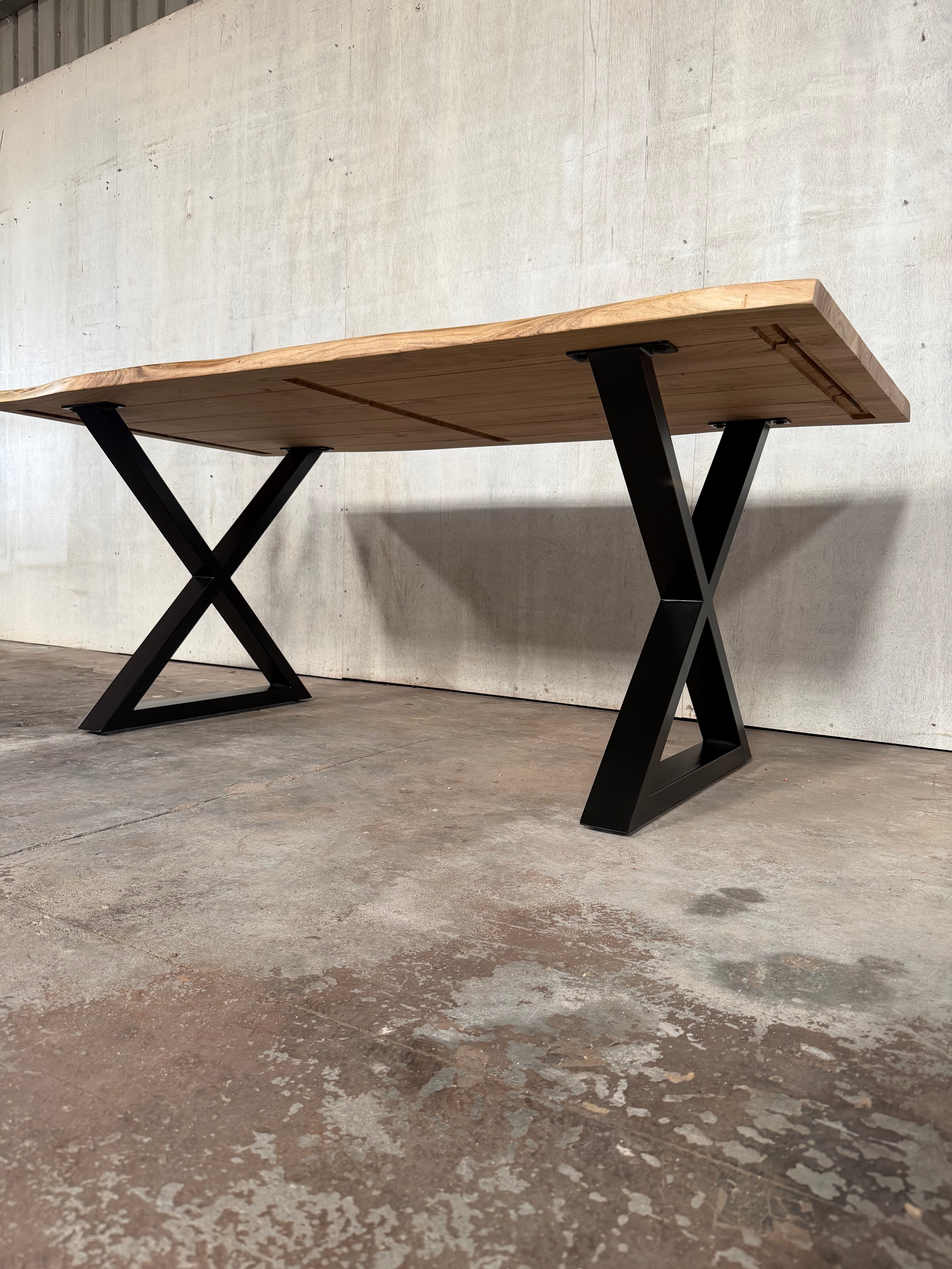 Wooden table with black metal legs against a concrete wall.