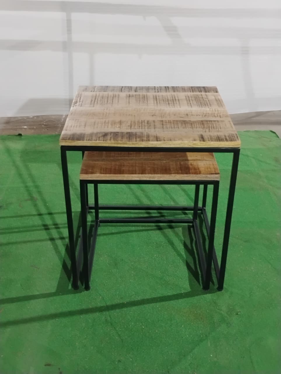 Two wooden tables with metal legs on a green floor.
